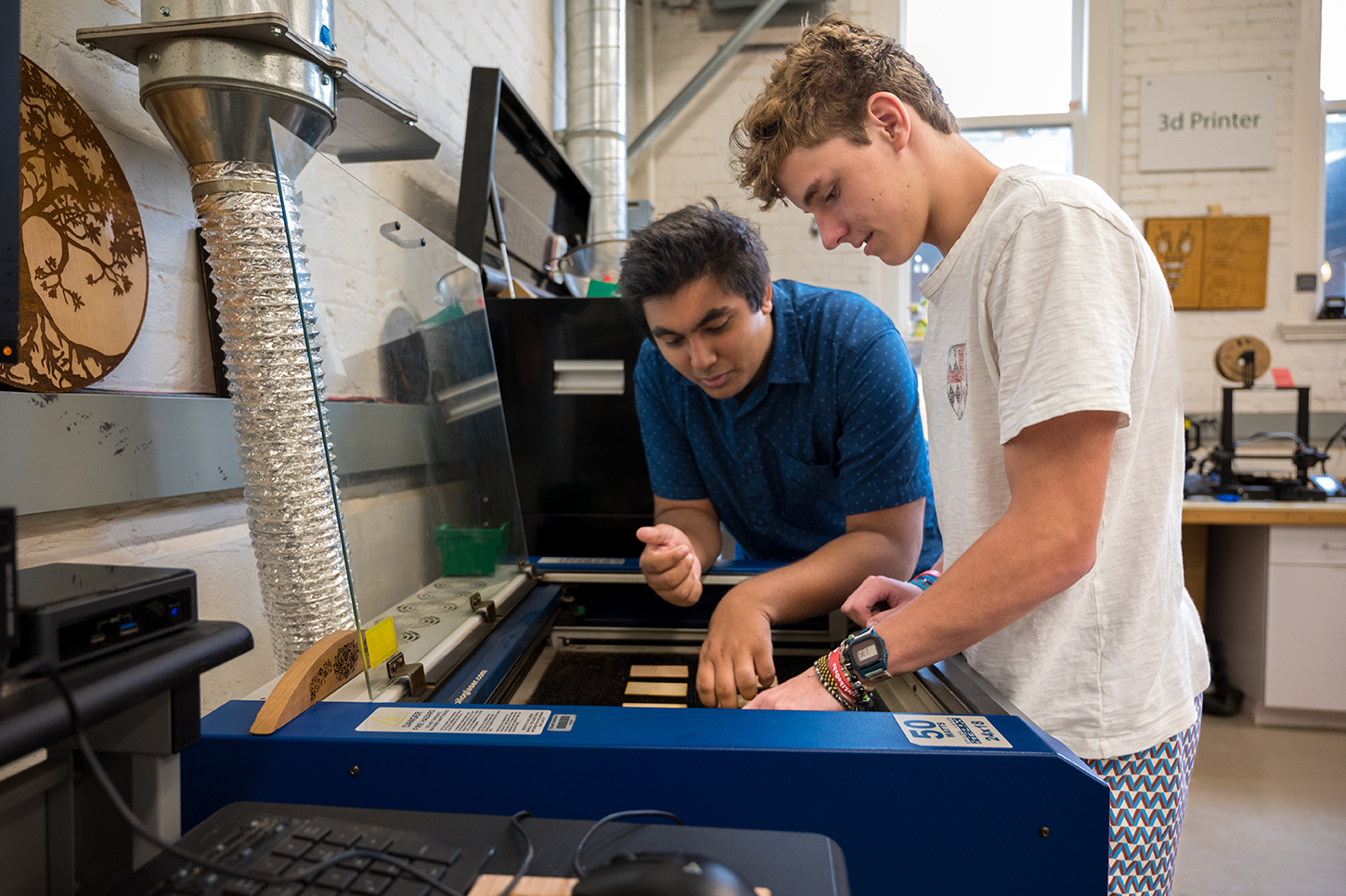 Two students use the lazer cutter in the Makerspace