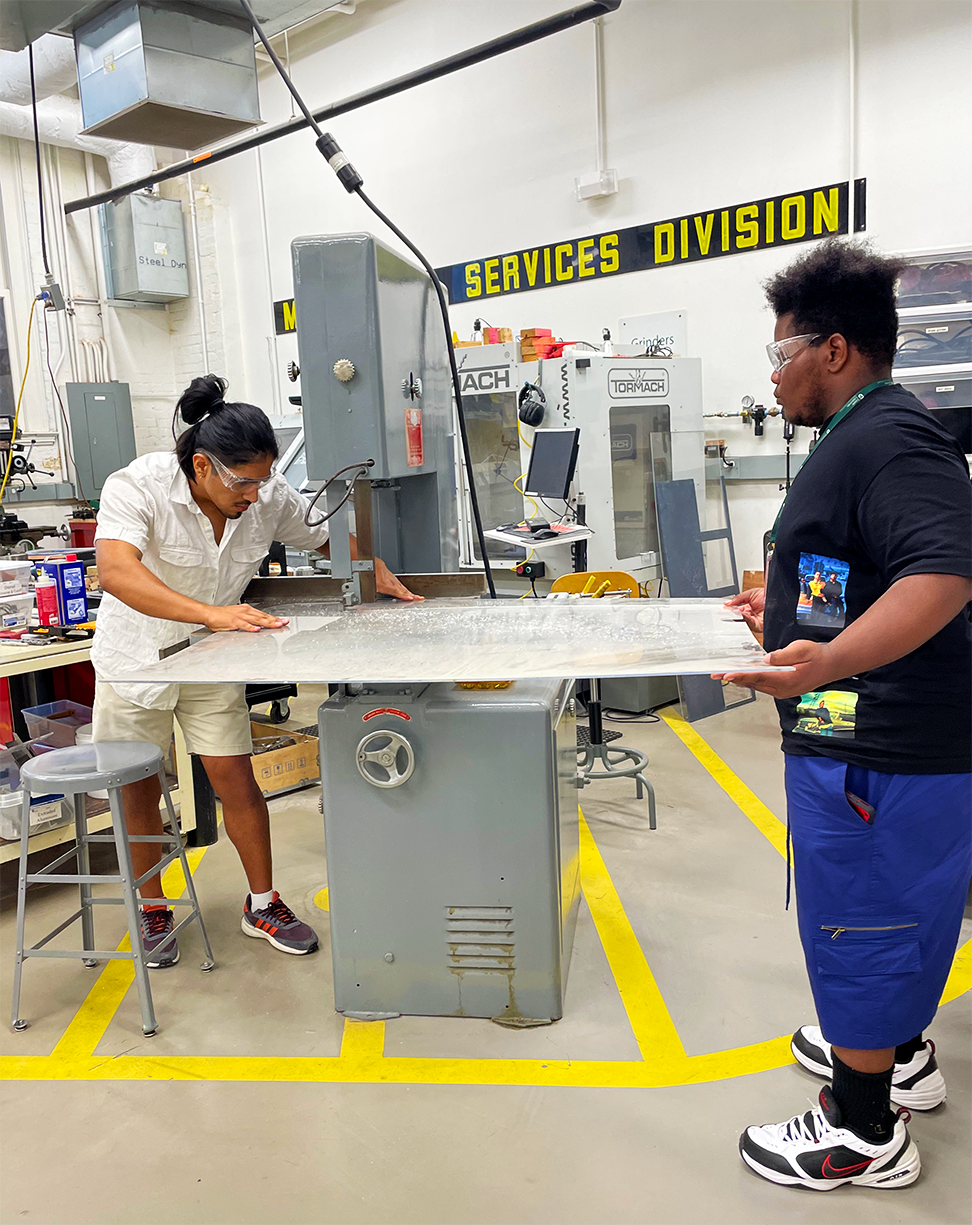 An Introduction to Engineering student works with a TA on a lathe in the Makerspace.