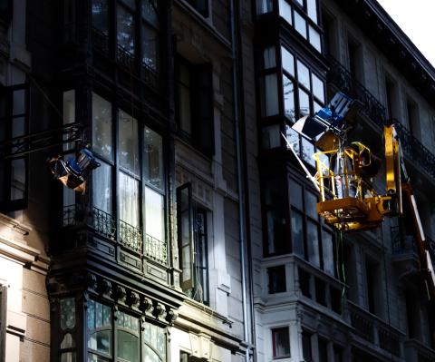 Film lighting rig on a yellow crane illuminates a building.