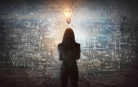 Silhouette of person looking at a glowing lightbulb above a wall of formulas.