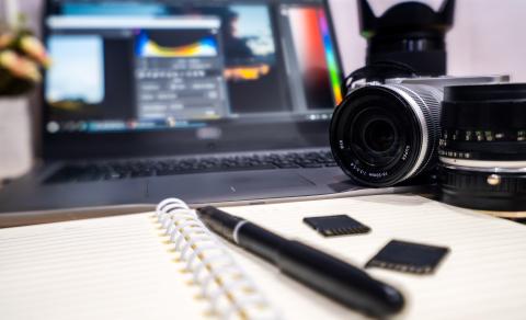 Camera, laptop with editing software, and a notebook with a pen.