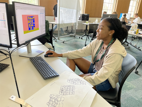 Pre-College architecture student smiles while working at a computer in a classroom.