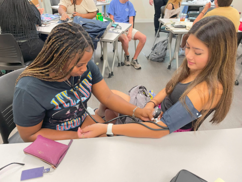 Two students practice taking blood pressure in a classroom.