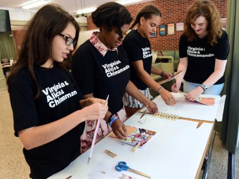 Pre-college students in black t-shirts work on project at a table.