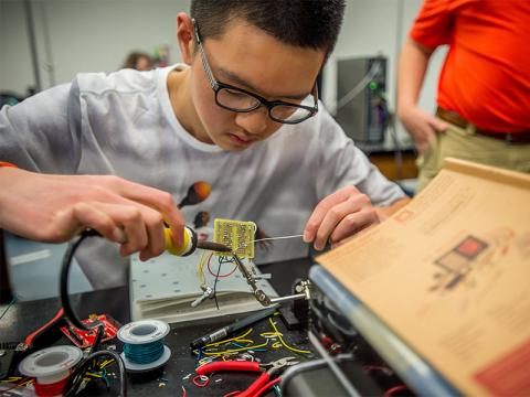 Pre-College student soldering a circuit board.