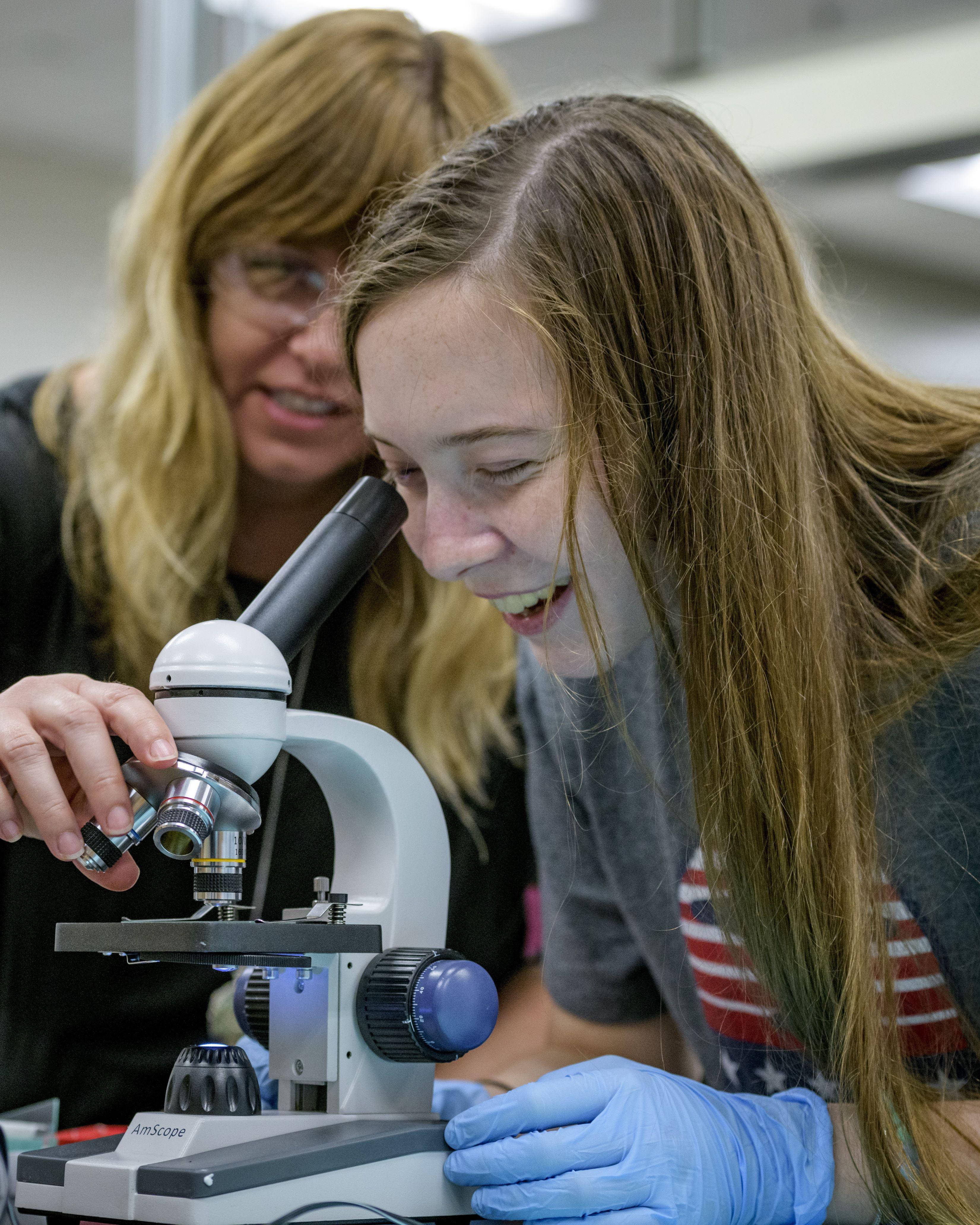 Student looking through a microscope with the help of a professor
