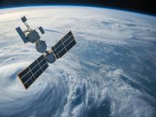 Space satellite with large solar panels orbits above a cloudy blue Earth.